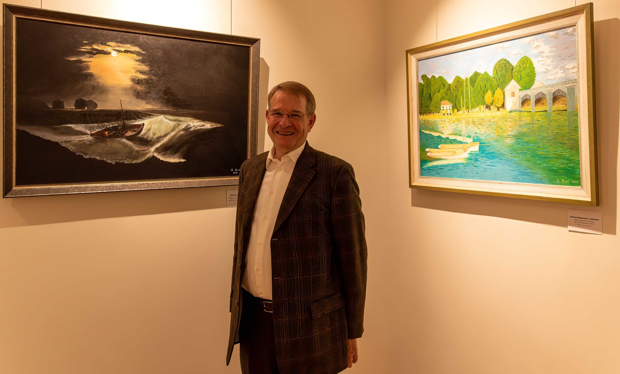 Dominique Binet à l’exposition Walferdange, debout entre deux de ses peintures.