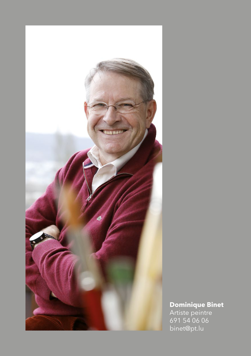 Portrait du peintre Dominique Binet vêtu en bordeaux, qui sourit à la caméra.